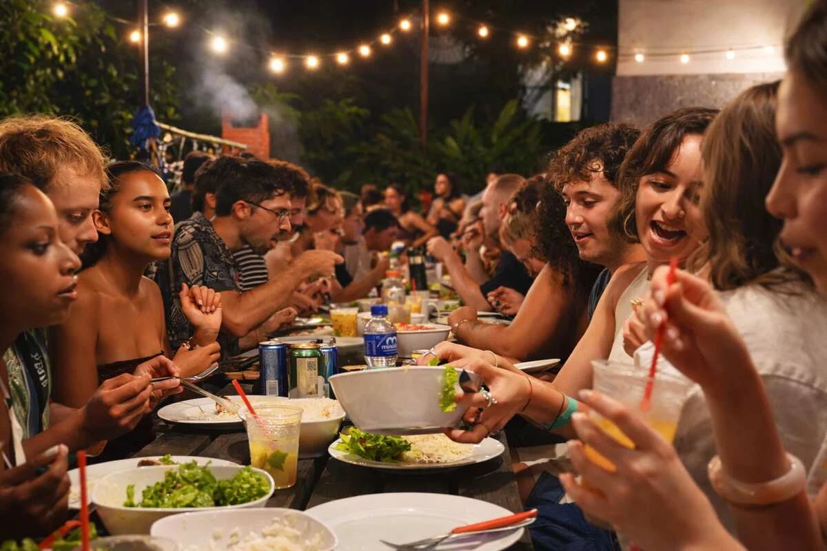 Travellers sharing a big table beneath the string lights